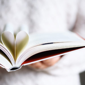 Book with opened pages and shape of heart in girl hands. Copy space. Love concept