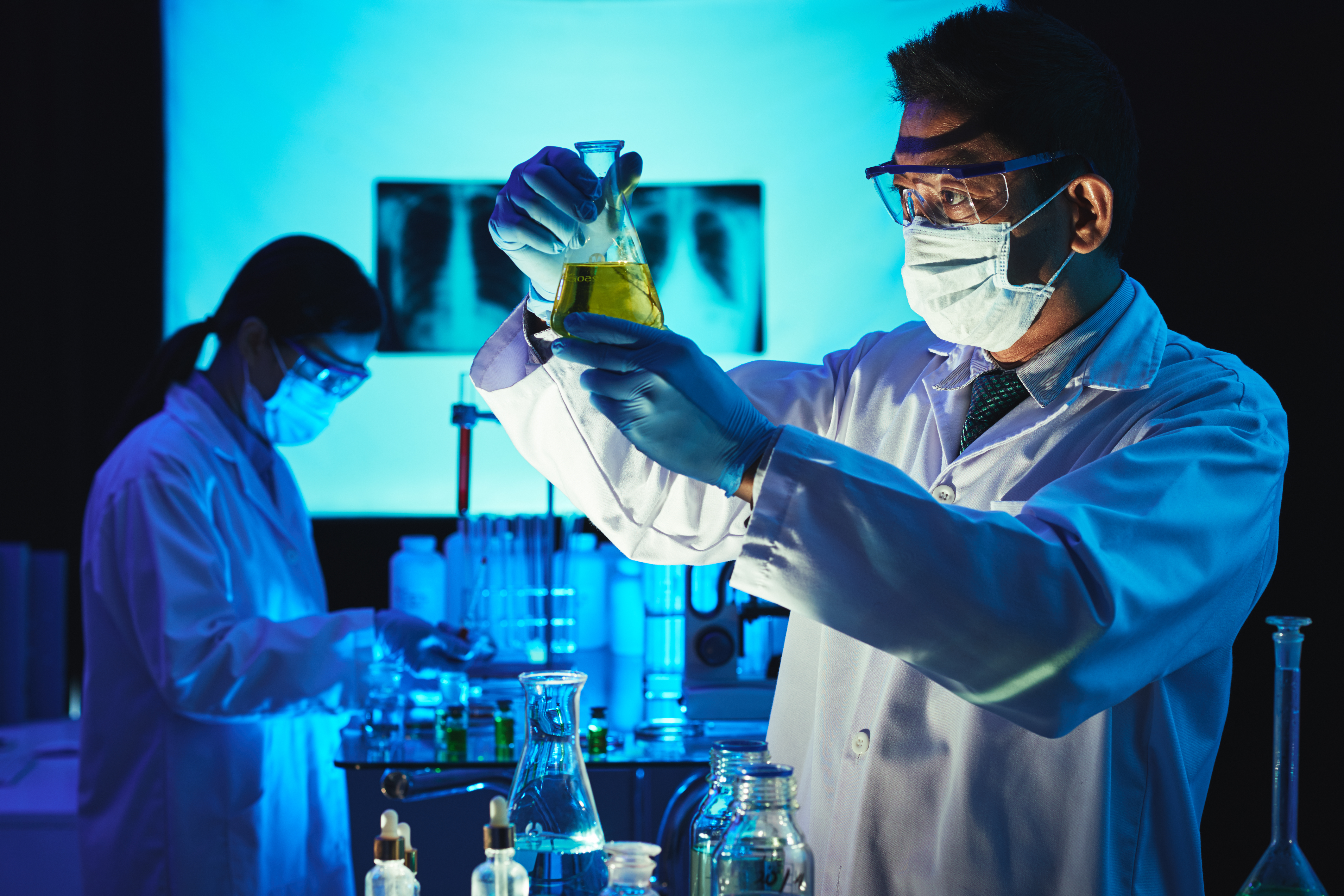 Vietnamese scientist looking at beaker with liquid in his hands
